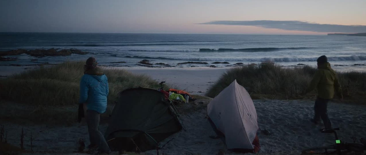 Two tents pitched above a beach at dusk, surf breaking beyond
