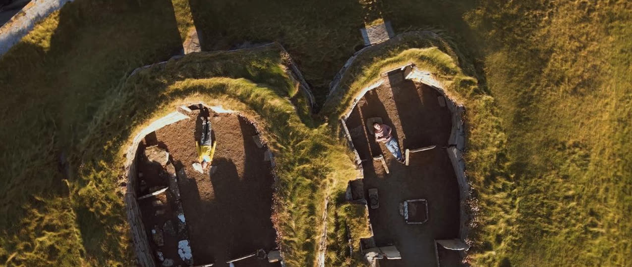 Looking straight down on two roofless stone croft houses, the riders inside