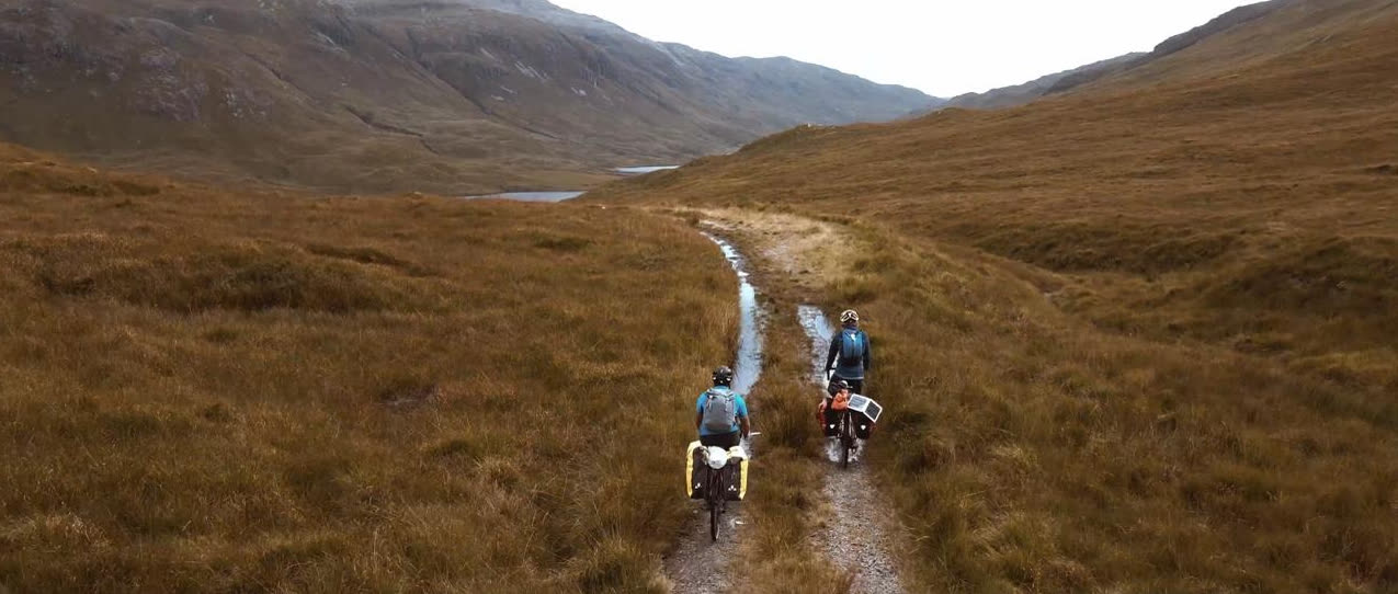 Two loaded bikes on a stony path winding up a Highland glen