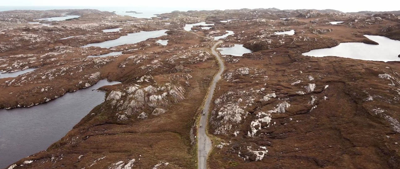 A single-track road threading between lochans across open moor
