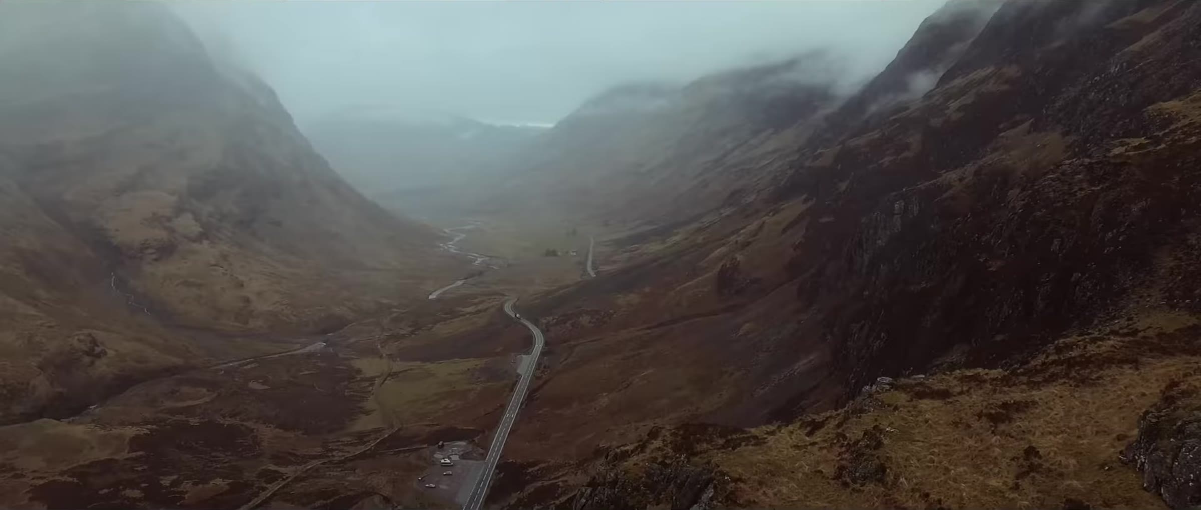 A road winding through a steep Highland glen under heavy cloud