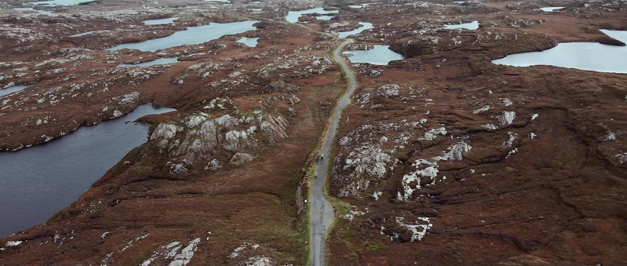 An aerial view of a single-track road threading between Hebridean lochans
